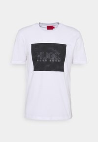 Bílý bavlněný tričko s obdélníkovým černým grafickým prvkem se nápisem "HUGO HUGO BOSS" v bílém písmu a texturovaným vzorem. Krátké rukávy.