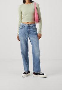 Světlězelený zkrácený top s dlouhým rukávem, volné světle modré džíny a černé tenisky s bílou podrážkou. Růžová taška visí přes rameno.