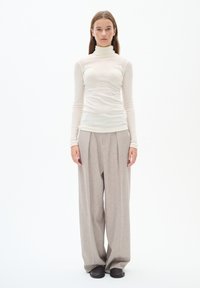 Light beige, long-sleeve turtleneck top, paired with loose, gray, pleated trousers and dark shoes; smooth fabric texture, minimalist design.