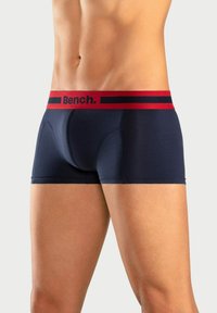 Temno modri bokserice iz mehkega materiala, ki imajo rdeč pas z logotipom "Bench." in kontrastnimi črtami.