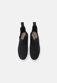 Svarta mocka slip-on skor med elastiska sidopaneler, vita gummisulor och en rund tå med subtila sömmar.