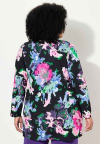 Top de manga larga con estampado floral que presenta un vibrante fondo negro con grandes patrones en rosa, púrpura, azul y verde, fabricado con un tejido suave y elástico.