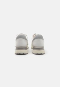 Zapatillas blancas y grises con parte superior de cuero suave, cuello acolchado y suela texturizada. Logo "GUESS" grabado en el talón.