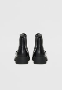 Czarne skórzane botki za kostkę o gładkiej fakturze, z zaokrąglonym noskiem i niskim obcasem. Minimalistyczny design z pętelkami z tyłu.