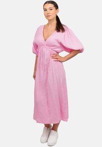 Roze A-lijn jurk met een diepe V-hals, poffende mouwen, geraffineerde taille en gestructureerde stof, gecombineerd met witte sneakers.