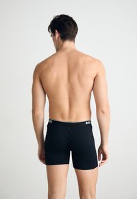 Schwarze Boxershorts mit elastischem Bund, der das "BOSS"-Logo zeigt. Glatter Stoff, taillierte Passform, minimale Nähte und Oberschenkellänge.