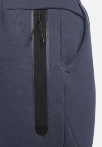 Marina blå sportbyxor med en sidoficka med dragkedja, svart mesh-kant och dragsko, tillverkade av ett mjukt, texturerat tyg.