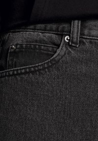 Svarta denimjeans med en slät yta, som har en liten framficka, en metallknapp och subtila diagonala mönster.