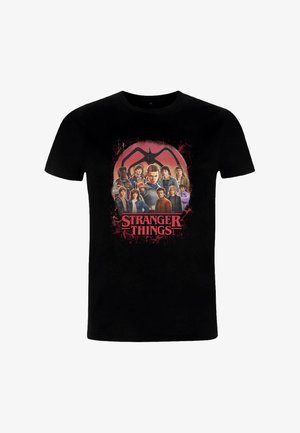Maglietta nera in cotone con una grande stampa grafica dei personaggi di "Stranger Things" con testo rosso, circondata da un elemento di design.