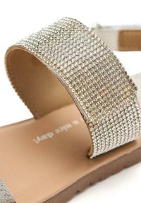 Sandal glitternato in argento con una cinghia testurizzata adornata di piccoli borchie, design open-toe e suola marrone. Rivestimento interno in pelle liscia.