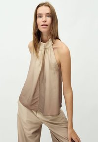 Top beige a scollo all'americana con fronte plissettato, realizzato in tessuto leggero; sfumatura di colore sottile, abbinato a pantaloni beige a gamba larga.