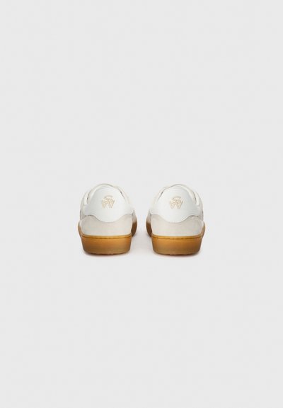 Baskets en daim blanc avec une semelle en caoutchouc crème. Présentent une forme arrondie et un petit logo surélevé en or sur le talon.