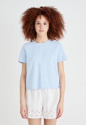 Lichtblauwe katoen t-shirt met korte mouwen en een ronde halslijn. Gepaard met witte shorts met golvende randen en stippen details.