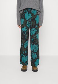 Wijde broek met bloemenpatroon in teal en zwart, gemaakt van zachte stof. Gecombineerd met bruine chunky schoenen en een grijze oversized trui.