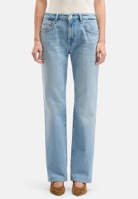 Jeans in denim azzurro chiaro a gamba dritta con vita media, 5 tasche e una sottile texture sbiadita, abbinati a scarpe marroni con punta a punta.