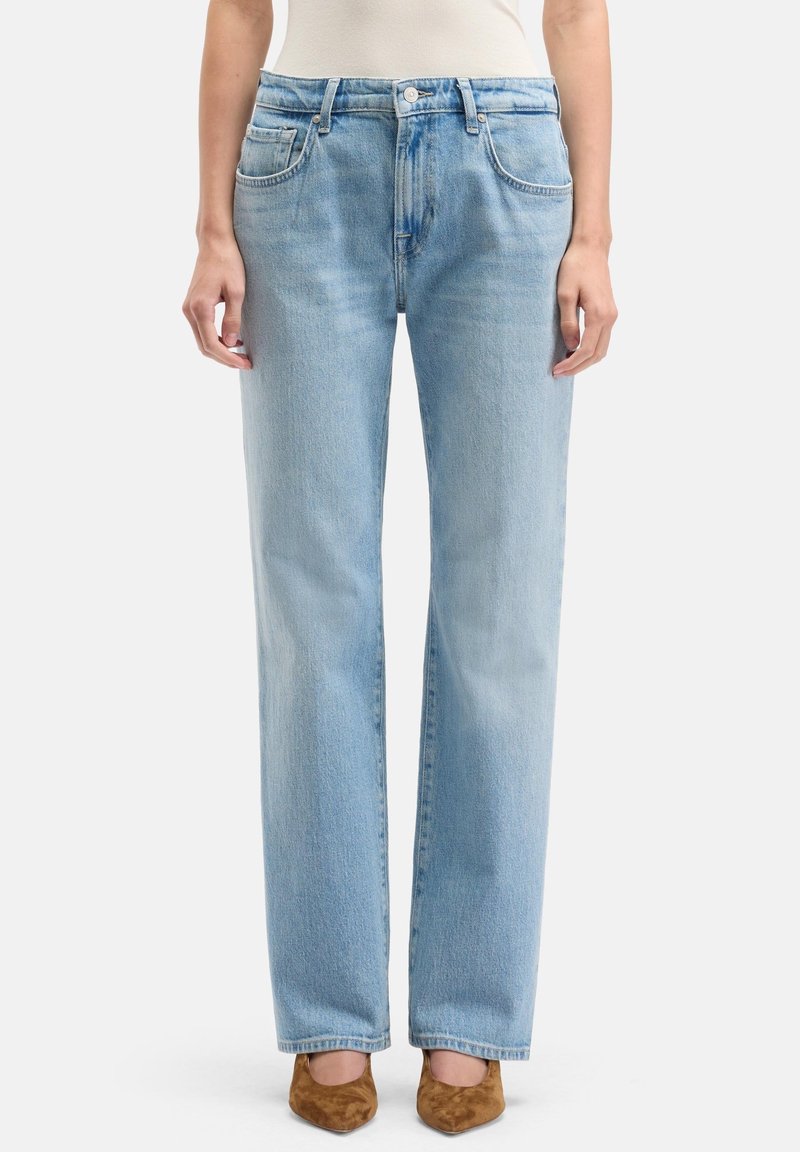 Jeans in denim azzurro chiaro a gamba dritta con vita media, 5 tasche e una sottile texture sbiadita, abbinati a scarpe marroni con punta a punta.