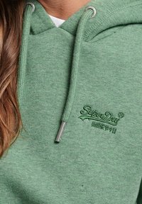 Felpa verde chiaro in morbido tessuto, con tasca frontale, coulisse e logo ricamato "SuperDry" sul petto.