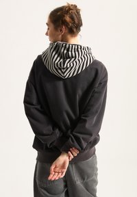 Zwarte sweatshirt met een gestreepte grijze en witte capuchon, voorzien van lange mouwen en een ontspannen pasvorm. De achterkant heeft een gladde textuur.