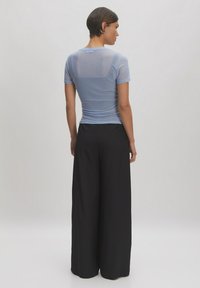 Lichtblauw doorzichtig kortmouwen shirt met een nauwsluitende silhouet, gecombineerd met zwarte ruime broek, wat de gladde textuur en casual stijl benadrukt.