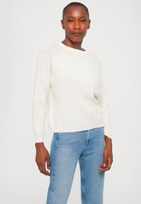 Kremfarget, lett genser med rund hals, raglanermer og en avslappet passform, kombinert med lyseblå denimjeans.