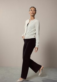 Šviesiai pilkas tekstūruotas kardiganas su apvaliu apykakle, derinamas su juodomis plačiomis kelnėmis ir sidabro spalvos papuoštais aukštakulniais.