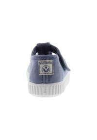 Scarpa slip-on in tela blu con suola in gomma bianca e dettagli cuciti. Etichetta del logo visibile sul tallone, con una finitura testurizzata.