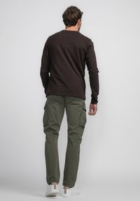 Chemise longue marron à manches longues, pantalon cargo vert avec poches sur les côtés, et sneakers blanches avec des accents beige, présentés de dos sur un fond uni.