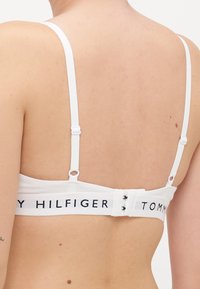 Bralette bianco in cotone con spalline regolabili, con fascia solida sul retro con il logo "TOMMY HILFIGER" in blu navy. Chiusura a due ganci.