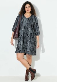 Robe noire et grise à motif serpent avec un décolleté en V, des manches trois-quarts et une silhouette évasée ; associée à des bottes décontractées marron.