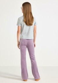 T-shirt gris à manches courtes associé à un pantalon évasé lavande. Le pantalon a une finition douce et texturée et est complété par des chaussures à semelle en bois.