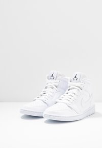 Zapatillas altas blancas con puntera perforada, cordones planos y logo bordado en la lengüeta. Textura suave con una suela de goma duradera.