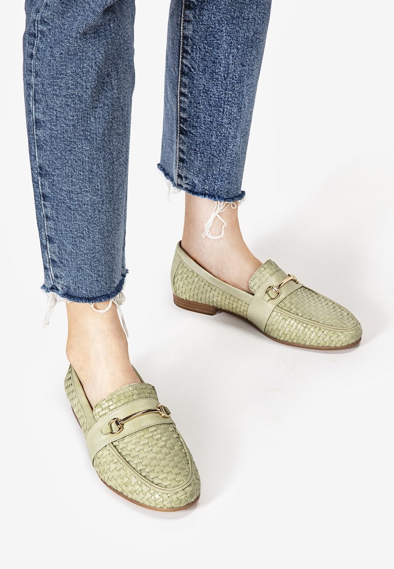 Mocassins en cuir vert clair tissés avec un détail doré portés avec un jean bleu à ourlet effiloché pieds nus.