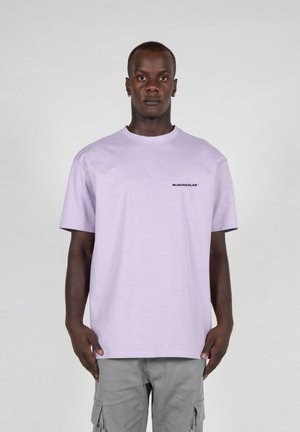 Lilac cotton t-shirt with short sleeves, round neck, and a small black logo printed on the chest. Worn with gray cargo pants.