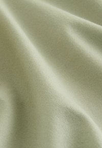 Gaiši zaļš audums ar gludu tekstūru un smalku aušanas rakstu, kas iezīmējas ar mīkstām krokām un salocījumiem, kas uzlabo tā taustes kvalitāti.