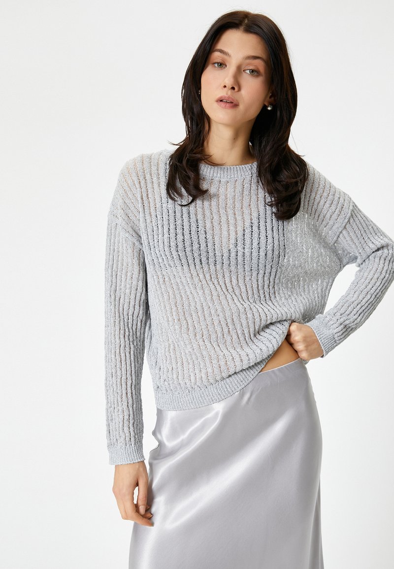 Maglione grigio chiaro, strutturato, con righe verticali, maniche lunghe e una vestibilità ampia, abbinato a una gonna in satin argentato liscia.