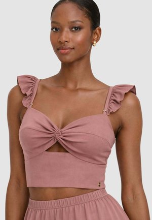 Donna che indossa un top corto malva con spalline arricciate e dettaglio a nodo intrecciato sul davanti, abbinato a pantaloni a vita alta coordinati.