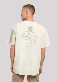 Cream-colored cotton t-shirt with short sleeves, featuring a geometric black graphic design on the back, showcasing various polygon shapes.