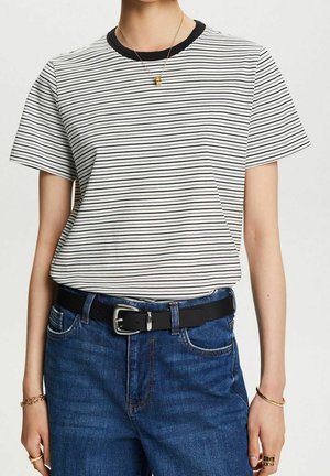 Persona con una camiseta de rayas blancas y negras, jeans azules con cinturón negro y joyas de oro que incluyen collar, pulseras y anillos.