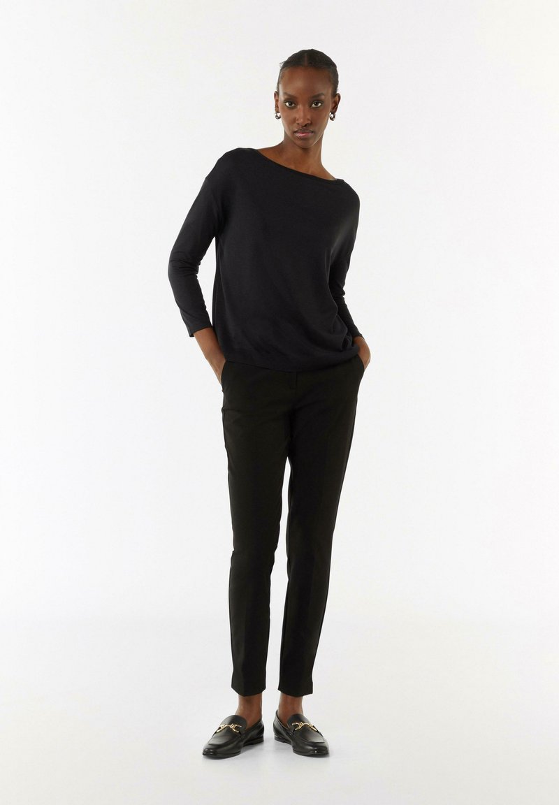 Zwarte langemouwen top, casual fit, bootlijn. Gepaard met strakke zwarte broeken en zwarte instappers met gouden accenten.