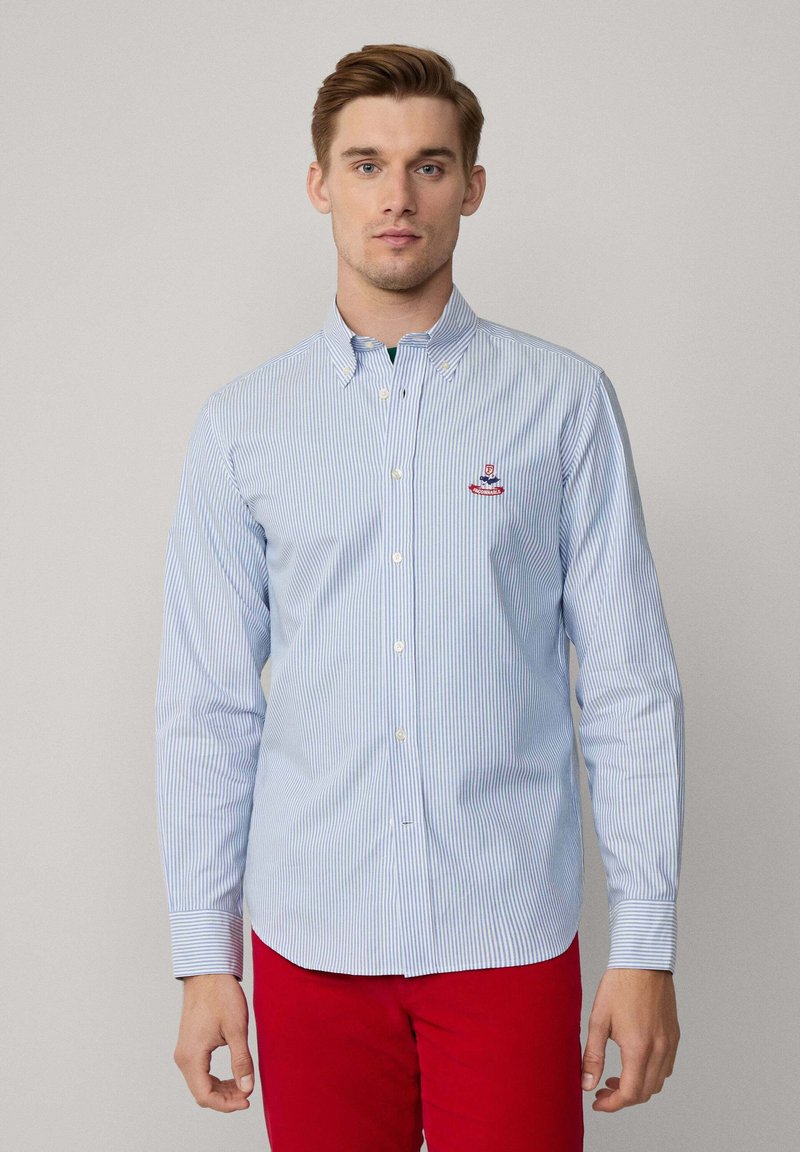 Camisa de botones a rayas azul y blanca con cuello, que presenta un logo bordado en el pecho. Mangas largas y diseño de dobladillo recto.