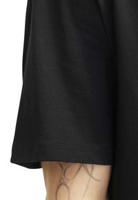 Camiseta de algodón negra con un corte relajado. Mangas cortas y una textura suave. El borde de la manga muestra un detalle de costura.