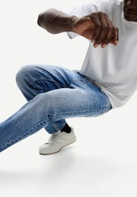 Blauwe denim jeans met een vervaagde textuur, gecombineerd met een eenvoudig wit t-shirt en witte sneakers, met een low-profile ontwerp en strakke lijnen.