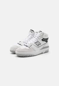 High-top basketball shoes in white leather with grey suede accents. Features perforations, black logos, and a rubber sole for traction.