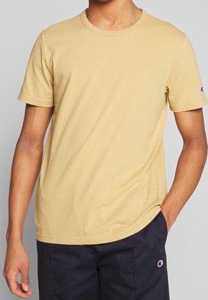 Żółta bawełniana koszulka z krótkimi rękawami, okrągłym dekoltem i naszywką z logo na rękawie. Gładka tekstura, regularny krój, minimalistyczny design.