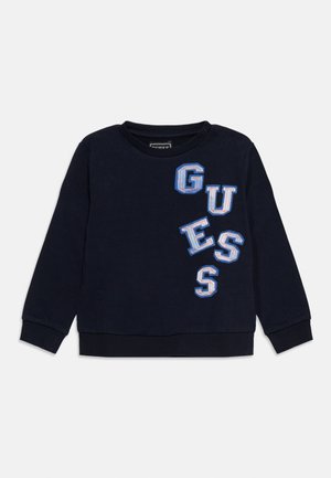 Bluza cu mâneci lungi, de culoare albastru marin, cu mansete și tiv cu dungi, având litere aplicate albe și albastre care formează cuvântul "GUESS" diagonal pe partea din față.