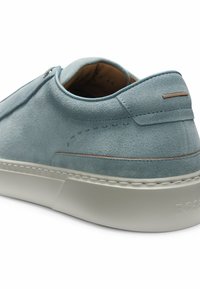 Sneaker in camoscio azzurro chiaro con suola bianca, cuciture dettagliate e delicato accento marrone sul tallone, vista da un angolo laterale posteriore.