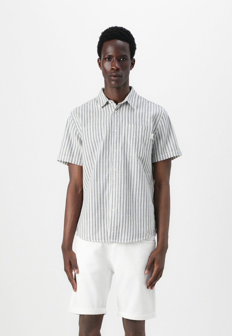 Camisa de botón de manga corta con rayas verticales azules y blancas, material de algodón, bolsillo frontal y textura suave. Combínala con pantalones cortos blancos.