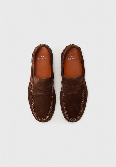 Mocassins en suede marron avec un design de style mocassin, présentant des coutures contrastées et une semelle intérieure en cuir lisse. Profil plat et style à enfiler.
