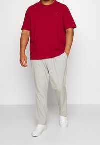 Red short-sleeve t-shirt, relaxed fit, paired with light gray textured pants and white sneakers. Simple, modern design with minimal branding.