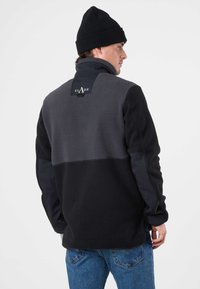 Giacca in pile con colletto alto, caratterizzata da blocchi di colore grigio e nero. Include un gancio per appenderla e un dettaglio logo sul retro.